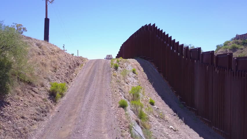CIRCA 2010s - U.S.-Mexico border - Rising aerial over a border patrol vehicle standing guard near the border wall at the US Mexico border at Nogales, Arizona.