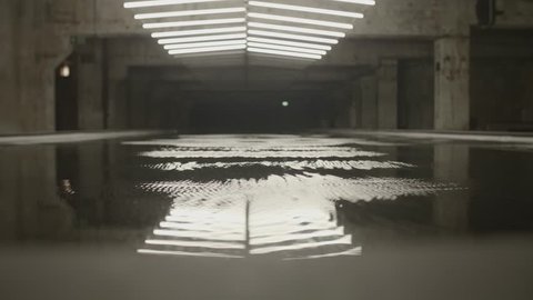 4k shot of white fluorescent lighting turn on and off and reflecting in the water or puddle in industrial building. Many neon lights blinking and flashing on the ceiling.