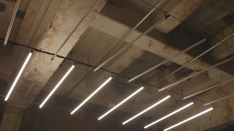 4k shot of white fluorescent lighting turn on and off and in industrial building. Many neon lights blinking and flashing on the ceiling.