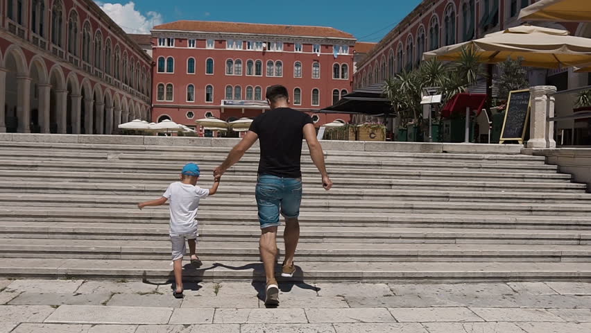 The father and his son have fun climbing up the stairs on Split's square. Croatia slow motion