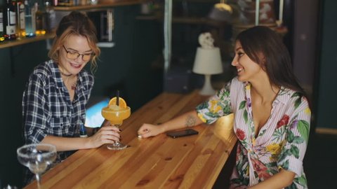 Two happy young female person standing bar counter talking each glass cocktail orange juice waitress barista barmaid amazing attractive woman beautiful dress smiling fun enjoy jouful cheerful speak