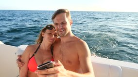 Happy loving couple, sitting together on yacht, taking selfies on his smartphone. 4k, slow motion
