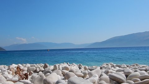 The transparent and turquoise sea in Saint John a beach of white stones, with blue sky and sun, in Ithaca island in Greece and Kefalonia in the background.