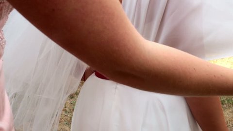 Bridesmaid checking lacing on happy bride's dress. Wedding celebration in summer. Wedding reception detail