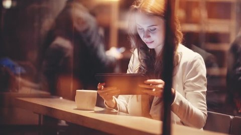Portrait of Young Woman Using Digital Tablet in Cafe at Night. 4K. Elegant businesswoman drinking coffee, reading news on tablet computer, using app, shopping, communicating in social media.