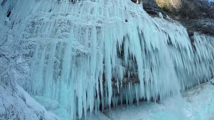 CLOSE UP Stunning frozen waterfall icicles on rocky mountain cliff on winter day. Winter cascade frozen into numerous white icicles. Waterfall falling past hundreds of icicles. Winter wonderland