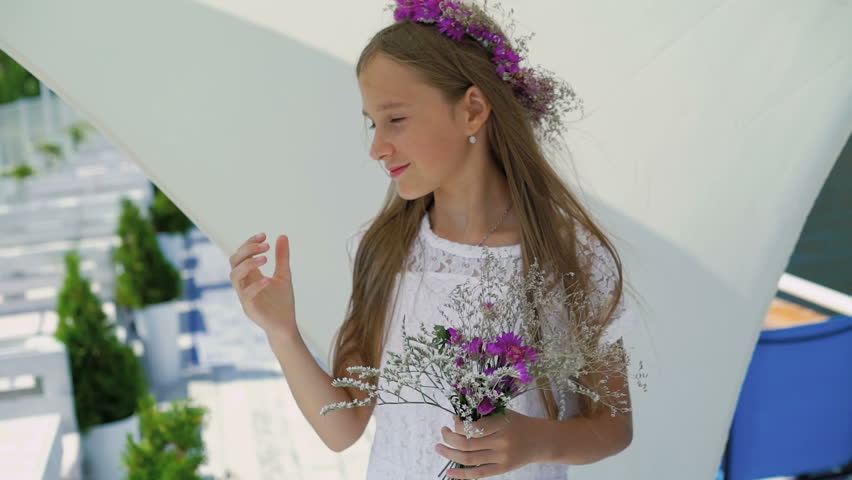 Happy young girl sniffing flowers in hands and smiling at bay bar. Slowly