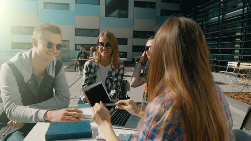Students wear sunglasses have pleasant break talk on table with laptop and books before modern building, cafe sunny day steady slowmotion Royalty-Free Stock Footage #31417621
