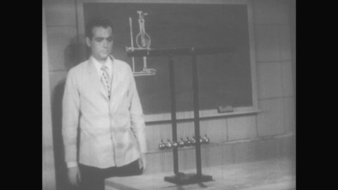 1950s: Man in suit approaches Newton's cradle, picks up leftmost ball and drops it. Newton's cradle in motion. Man stops motion in Newton's Cradle, and then resumes it.