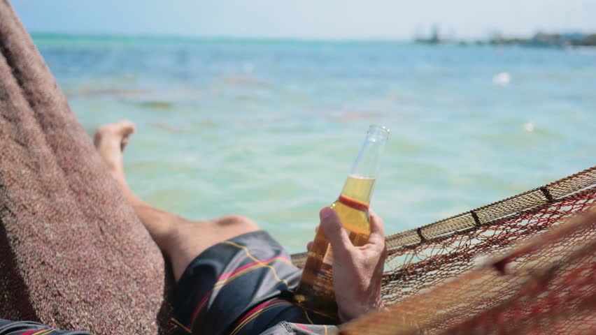 Man drinks a beer resting in hammock of the caribbean beach, Mahahual, Mexico. 4k.