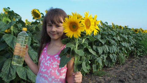 Child in the field of sunflowers with a bottle of sunflower oil. A little girl with a bouquet of sunflowers and a bottle of oil.