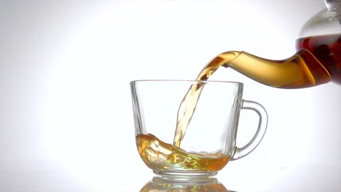 Tea pouring. Tea being poured into glass transparent tea cup. Tea time. Transparent glass teapot and teacup. Slow motion 240 fps. 4K UHD video 3840X2160