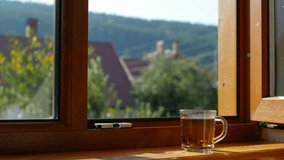 Cup of tea on the window sill. Morning tea in glass cup. View on mountains with forest from the window. Calm scene of early morning. New day with cheerfulness. Autumn morning concept