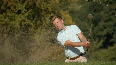A Celebrating Golfer hits a golf ball out of a sand trap with exploding sand in slow motion, drops the ball into the cup and celebrates looking skyward. 