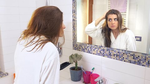 Woman in bathroom horrified by receiding hairlines desperate