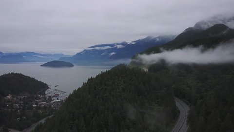 Aerial view of Horseshoe Bay and Sea to Sky Highway in West Vancouver, British Columbia, Canada. Taken during a wet and rainy summer day with an overcast sky covered in low clouds.
