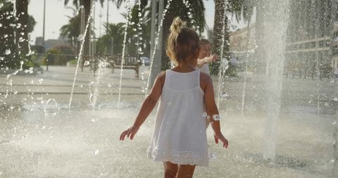 
little girls in town play with water in the fountains, happy and carefree, concept of freedom and happiness in childhood, starting summer and tourist cities.