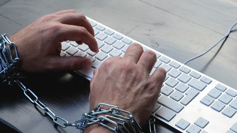 Businessman hands tied with chains on wrists typing on laptop keyboard
