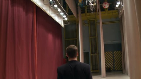 View from the back, the artist comes out behind the scenes onto the stage with a microphone and starts to sing