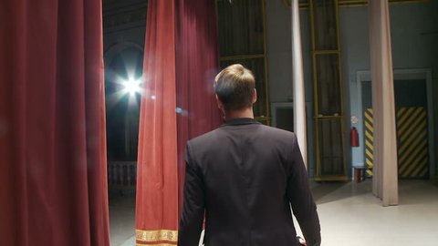 View from the back, the artist comes out behind the scenes onto the stage with a microphone and starts to sing