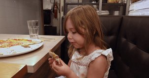 4k video. Four years age blonde girl eating pizza, very fast, sitting in black leather sofa at restaurant
