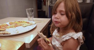 4k video. Four years age blonde girl eating pizza and dancing, sitting in black leather sofa at restaurant
