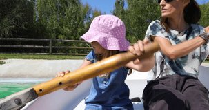 4k video. Four years old blonde child paddling next to woman mother sitting in boat at park lake 
