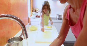 4k video. Four years old blonde child in the kitchen in teamwork with woman preparing raw potatoes to cook
