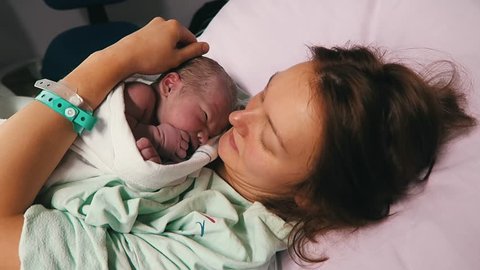 Childbirth. Mother holding her newborn baby child after labor in a hospital. Mother giving birth to a baby boy. Parent and infant first moments of bonding.