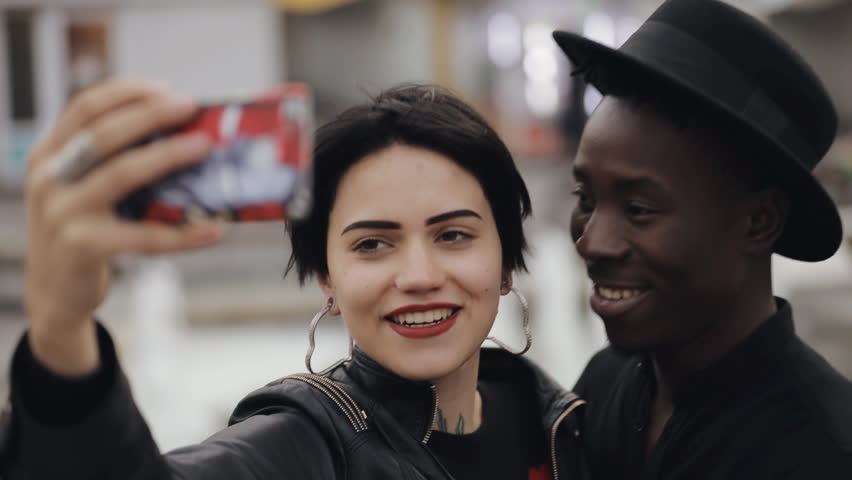 Slow motion of white woman and black man couple making a selfie video on smartphone. He kiss her cheek. They smiling, laughing together. Royalty-Free Stock Footage #31464793