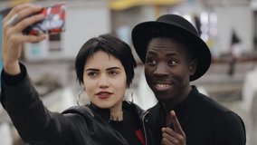 Slowmotion of white woman and black man couple makes selfie video on smartphone. They smiling, grimacing, laughing together.