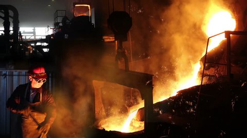 Hard work In foundry, melting iron, steel mill. Workers controlling iron smelting in furnaces, too hot and smoky working environment