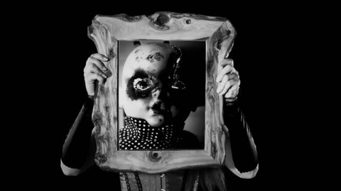 A sexy girl holding a wooden frame with a scene: a haunted doll, eyes burned, looking at the viewer, on a moving rocking chair. Scary Halloween horror black-and-white shot.
