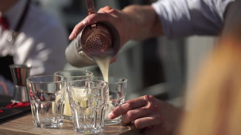 slowmotion shot of a bartender in an outdoor bar pours a cocktail into a glasses.