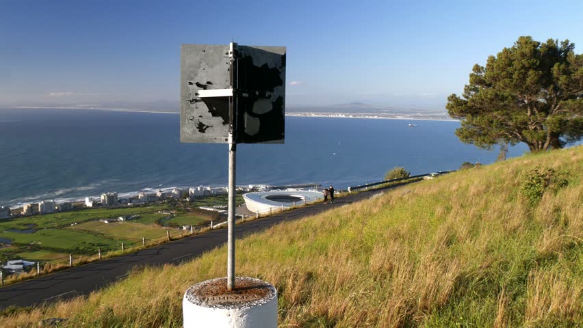 POV circling Signal Hill trig point marker with panning panoramic of Green point aerial with coastline, ocean horizon, Robben Island