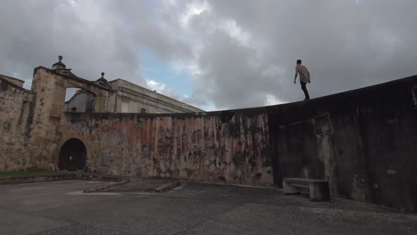 Hipster young man walks along beautiful old wall in San Juan, Puerto Rico. Shot in slow Motion