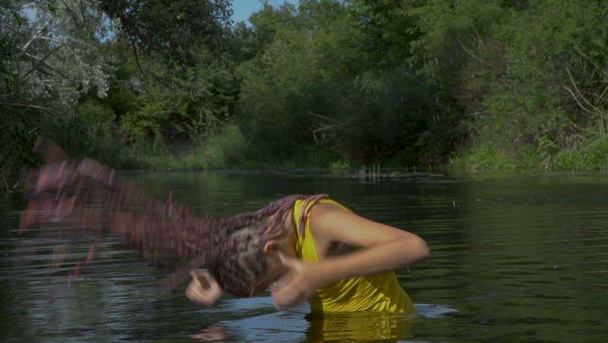 The girl emerges from the river. With her hair fall splashes of water. Slow motion