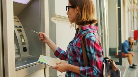 Attractive young woman with a city map in hands is inserting a credit card to withdraw some money.travel, commercial, people, shopping, personal, safety, client, enter, keypad, attractive, savings, 
