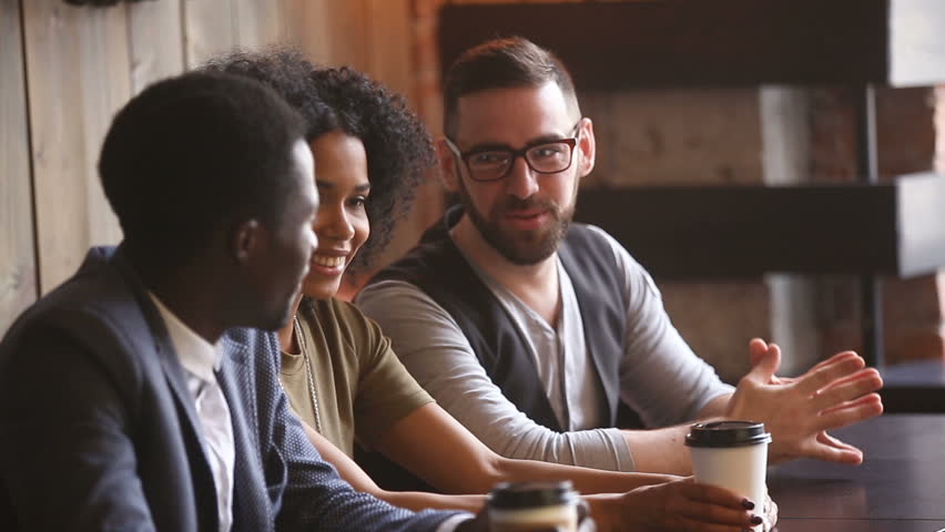 Young couple coming at meeting in cafe, man introducing new girlfriend to multiracial friends, girl getting acquainted with diverse mates of guy she dating, making first impression, nice to meet you