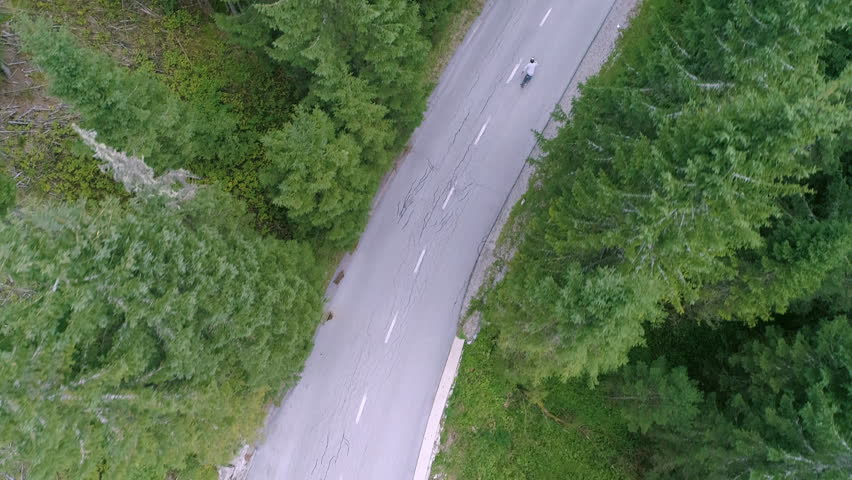 Aerial - Top down tracking shot of male longboarding on a road through the forest