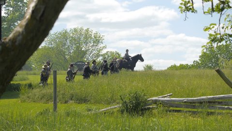 VIRGINIA - MAY 2017 - large-scale, epic Civil War anniversary reenactment -- in the middle of battle. Confederate ride horses past snake-rail fences and across tall grass field with swords and muskets