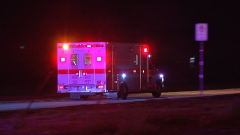 Ambulance drives down long road at night with flashing lights while transporting a patient.