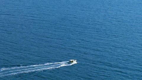 Boat moves on the sea, aerial view. Aerial view of small boat flowing in sea, travel and vacation concept. Aerial view of luxury speed boat cruising in ocean. One boat in the blue sea. Static camera.