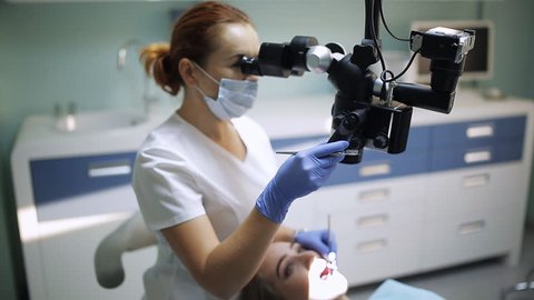 Female dentist with dental tools - microscope, mirror and probe treating patient teeth at dental clinic office. Medicine, dentistry and health care concept. Dental equipment
