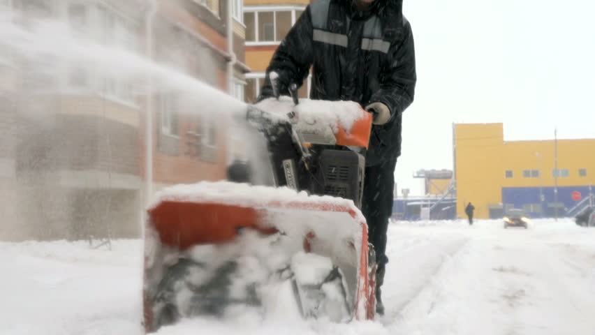Winter cleaning. Unknown man in overalls removing snow with snow plow machine in residential micro district in winter
