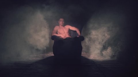 Sexy man sits in an armchair in smoke. The light appears and goes out