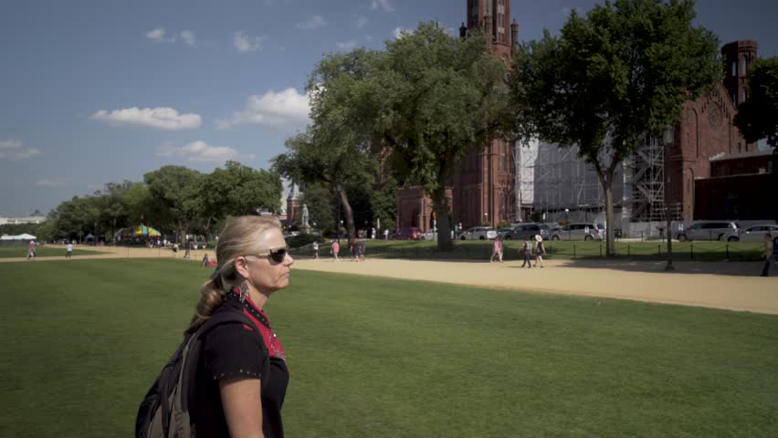 Steadicam shot of a mature woman wearing hip, ethnic dress walking on the National Mall with the US Capital and the Smithsonian Institution Castle in the