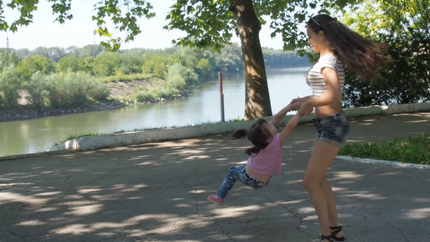 A teenage girl is turning a child. A happy girl is turning a little girl.