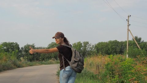 A young girl with a backpack is hiking. Hitch-hiking. The girl is trying to stop the car.
