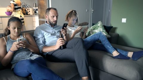 Family sitting on sofa and using tablet and smartphone at home
